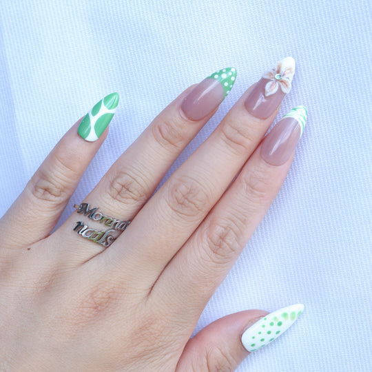 Leaf Dance press-on nails worn on hand, with muted sage green polka dots, wavy French tips, and a 3D flower on a nude base.