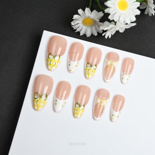 Lemon Lace press-on nails laid out with nude bases, white French tips, yellow gingham bows, and lace edging in a cottagecore style