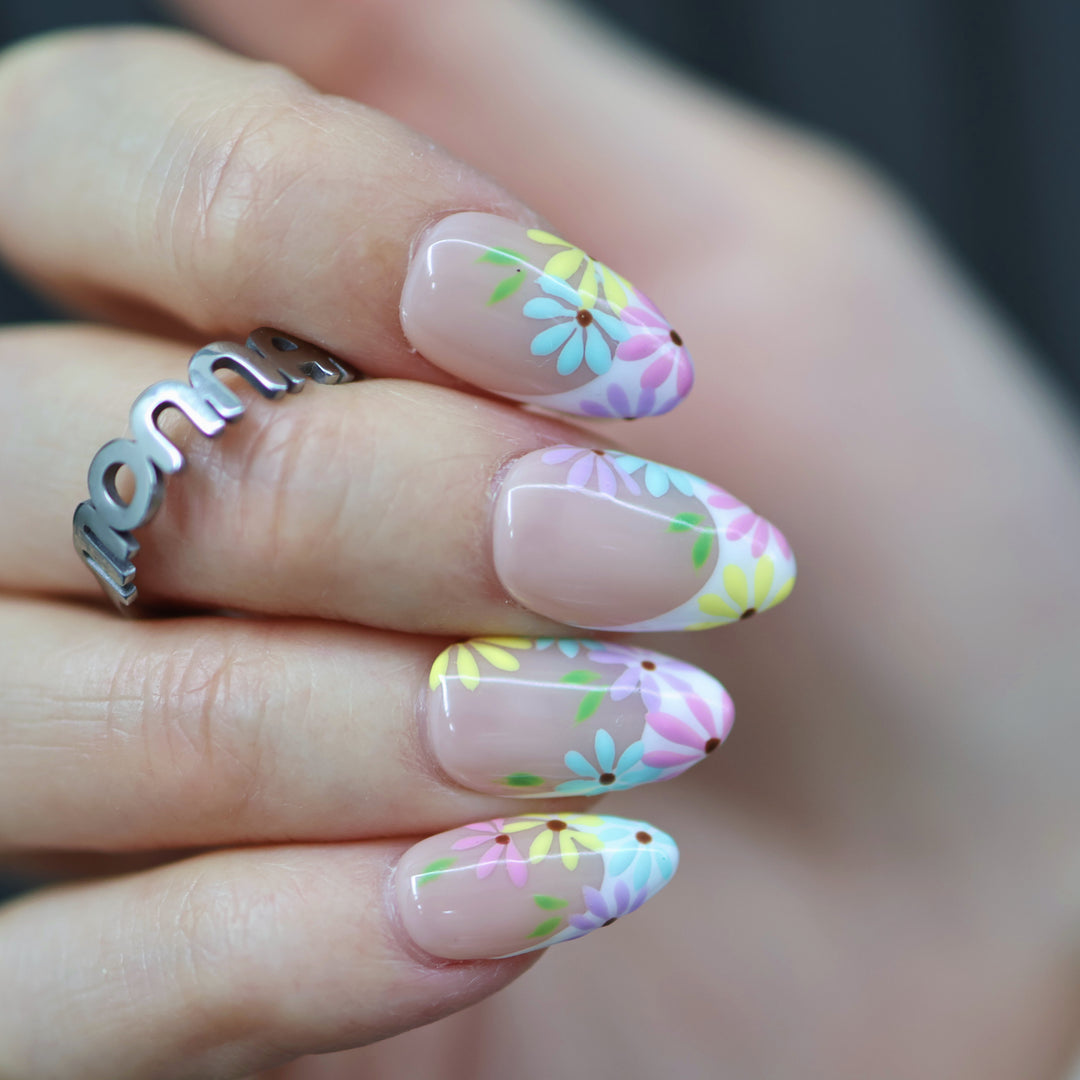 Little Daisy press-on nails on hand, nude base with pastel daisy floral French tips and glossy finish