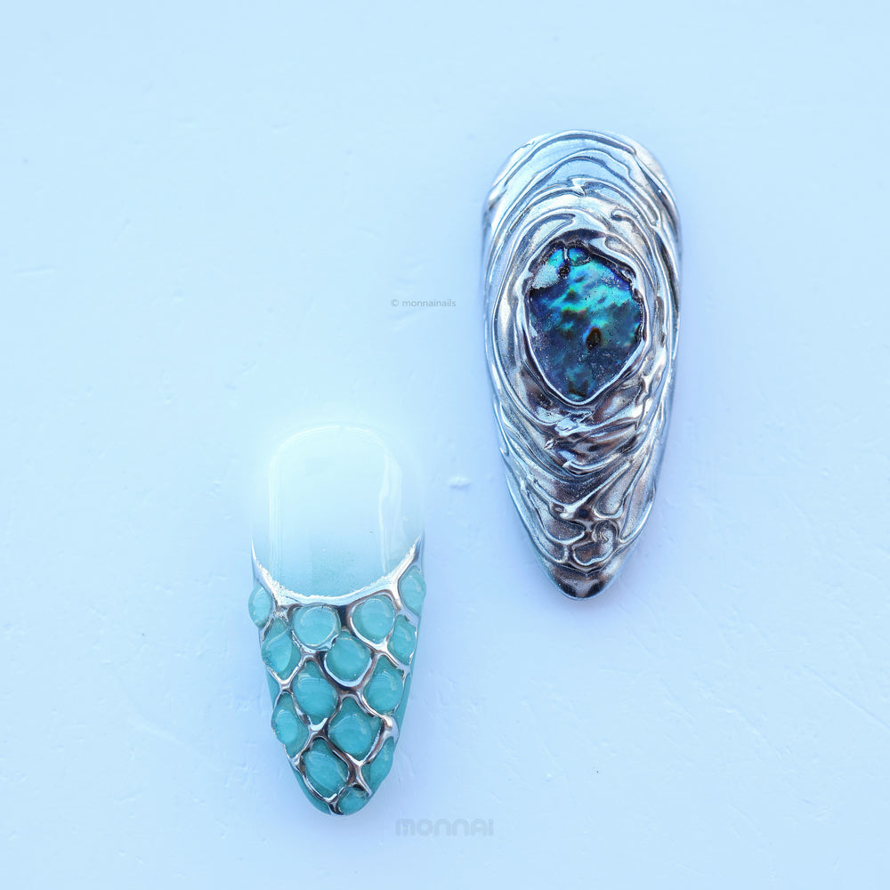Lost Atlantis press-on nails laid out close-up, with sculpted shell shapes, ocean blues, pearl-like accents and chrome details.