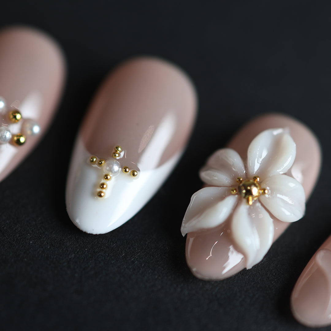 Love Story press-on nails in close-up, sheer nude and white French tips with 3D floral petals and gold bead accents