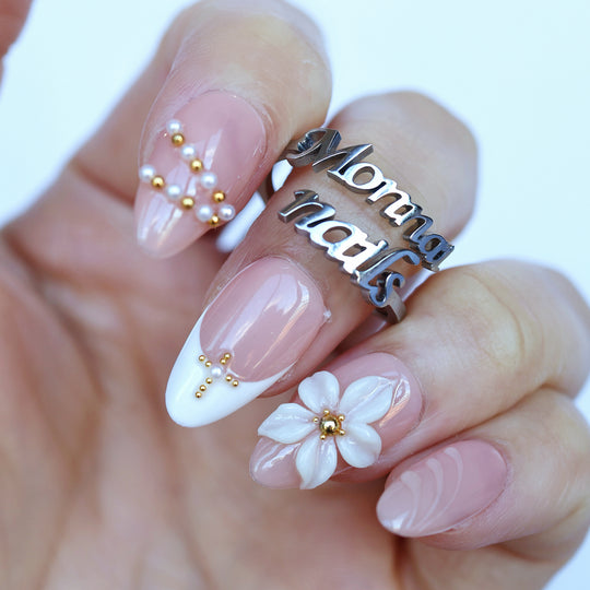 Love Story press-on nails on hand, sheer nude French tips with 3D white floral petals and pearl-gold bead accents