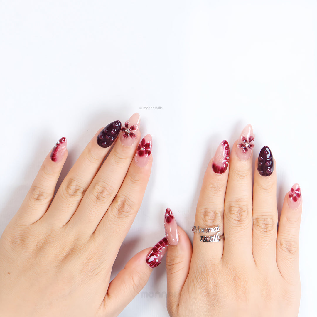 Lover’s Kiss press-on nails on hands, sheer nude pink with burgundy florals, 3D droplets and silver beads