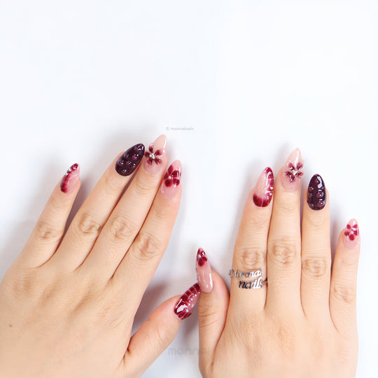 Lover’s Kiss press-on nails on hands, sheer nude pink with burgundy florals, 3D droplets and silver beads