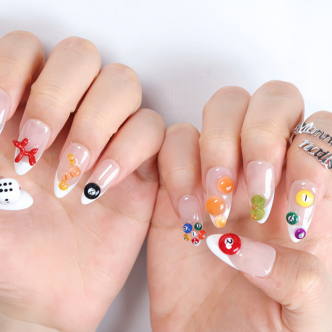 Lucky Numbers press-on nails worn on hands with sheer nude French tips, colorful billiard balls, dice, and glossy Y2K game-inspired details.