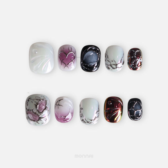 M-Code Cyber-Goth Rebellion press-on nails shown laid out, with iridescent silver, purple, black, and multichrome heart and thorn details.
