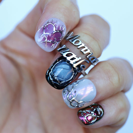 M-Code cyber-goth rebellion press-on nails in close-up, with purple aura, chrome heart motifs and metallic multichrome accents