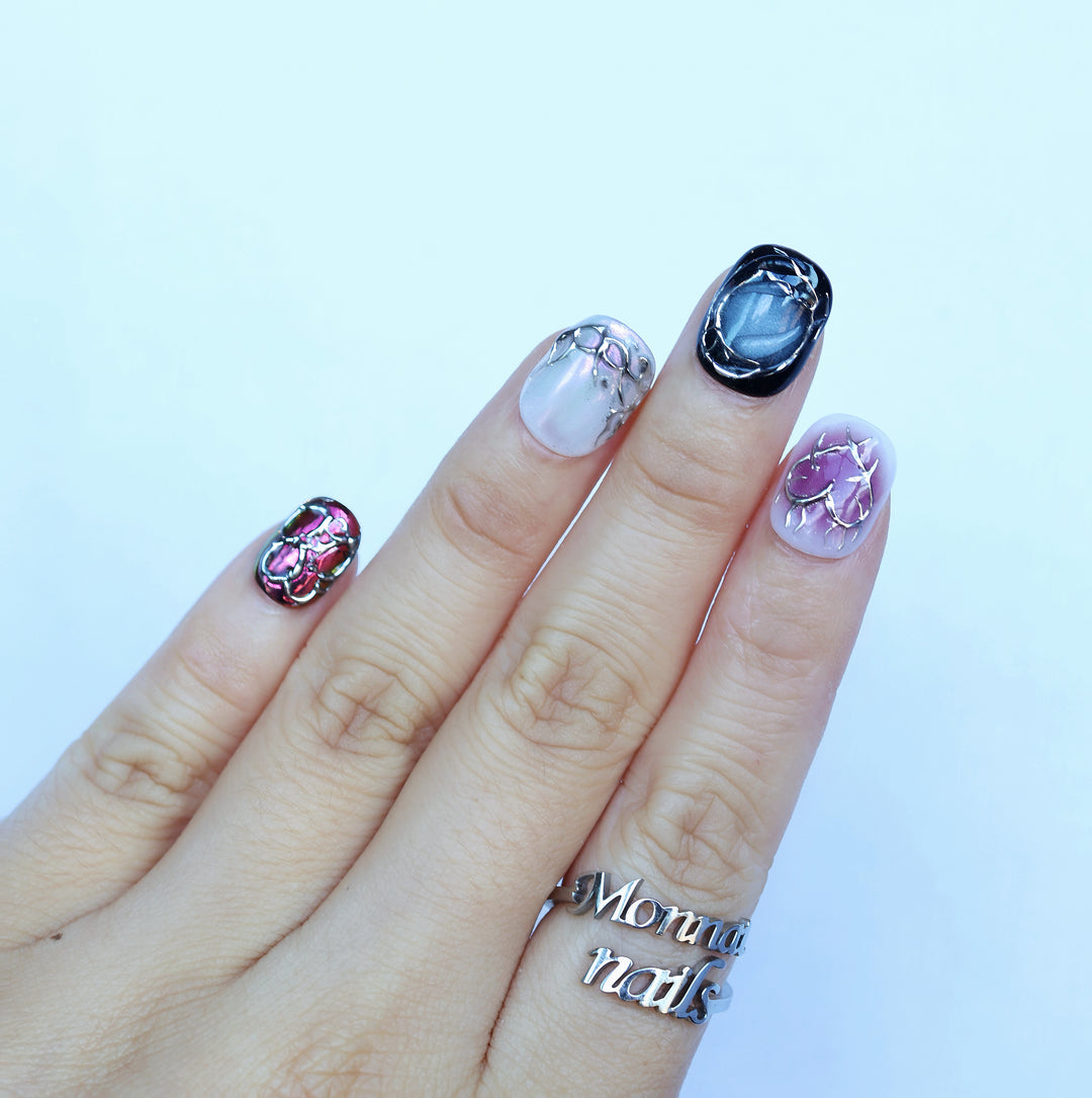 M-Code cyber-goth rebellion press-on nails on hand with chrome thorns, purple aura, and multichrome accents