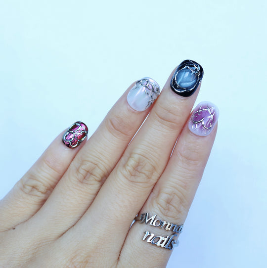 M-Code cyber-goth rebellion press-on nails on hand with chrome thorns, purple aura, and multichrome accents