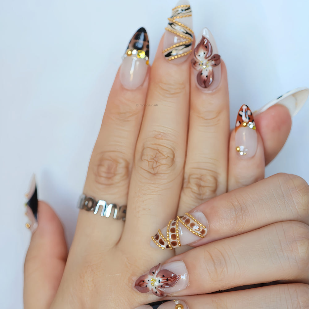 Madam Cheetah press-on nails worn on hand, with nude base, leopard accents, floral details and gold embellishments