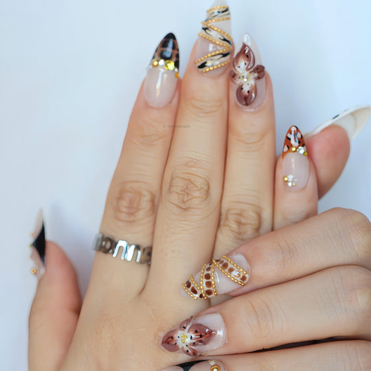 Madam Cheetah press-on nails worn on hand, with nude base, leopard accents, floral details and gold embellishments