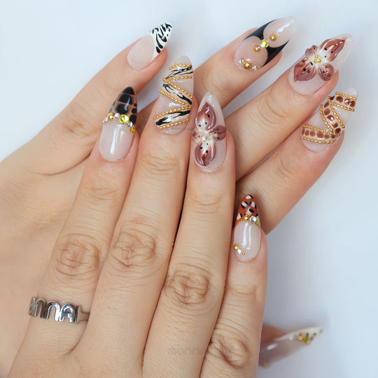 Madam Cheetah press-on nails on hand, sheer nude base with leopard, zebra and floral accents, gold chains and rhinestones.
