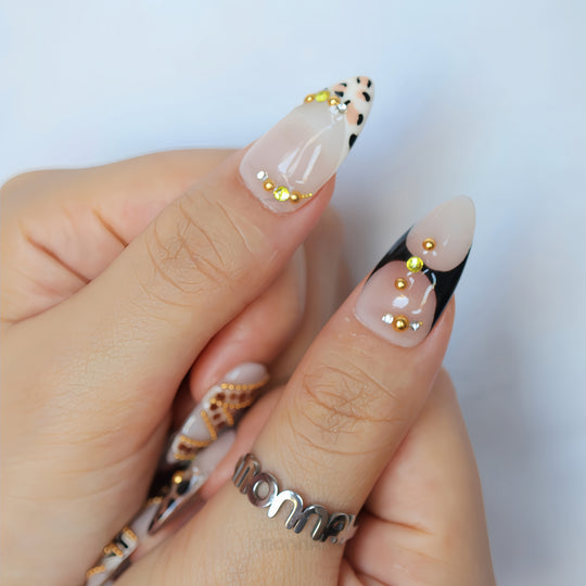 Madam Cheetah press-on nails worn on hand, nude with leopard accents and gold rhinestones in a glossy, playful glam look.