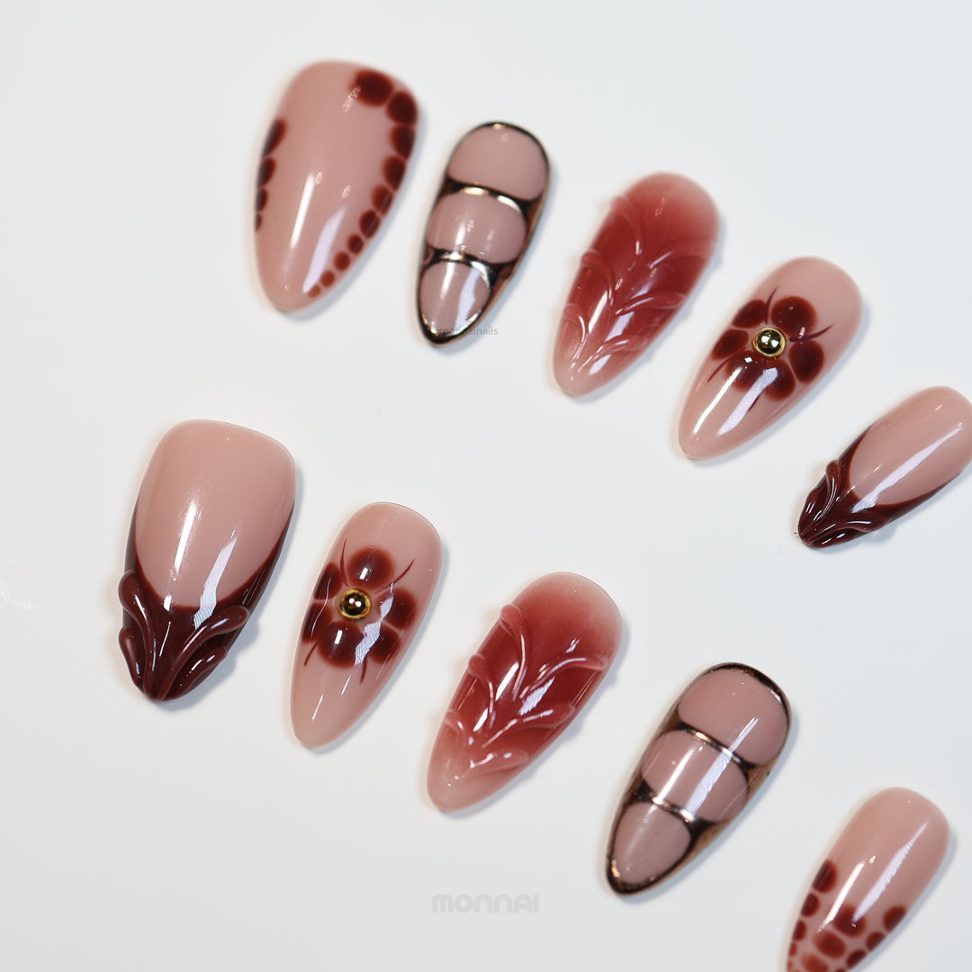 Maple Glow press-on nails laid out in close-up, with nude bases, rich brown accents, floral details, and glossy vintage styling.