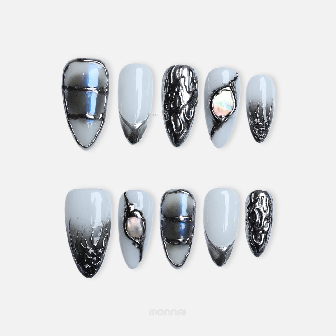 Metal Blaze press-on nails laid out in cool grey with chrome edging and iridescent inlay, plus sculpted accents.