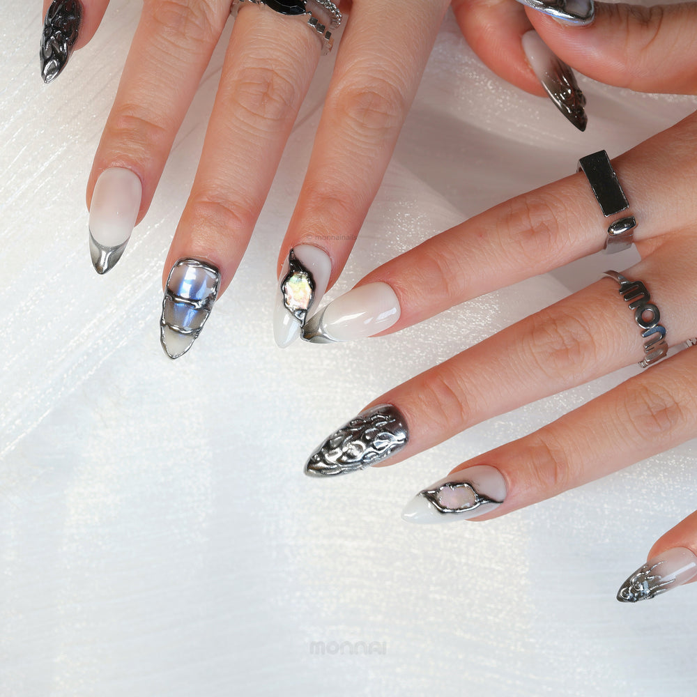 Metal Blaze press-on nails on hands, shown in close-up with chrome flame accents, sheer white bases, and sculpted silver details.