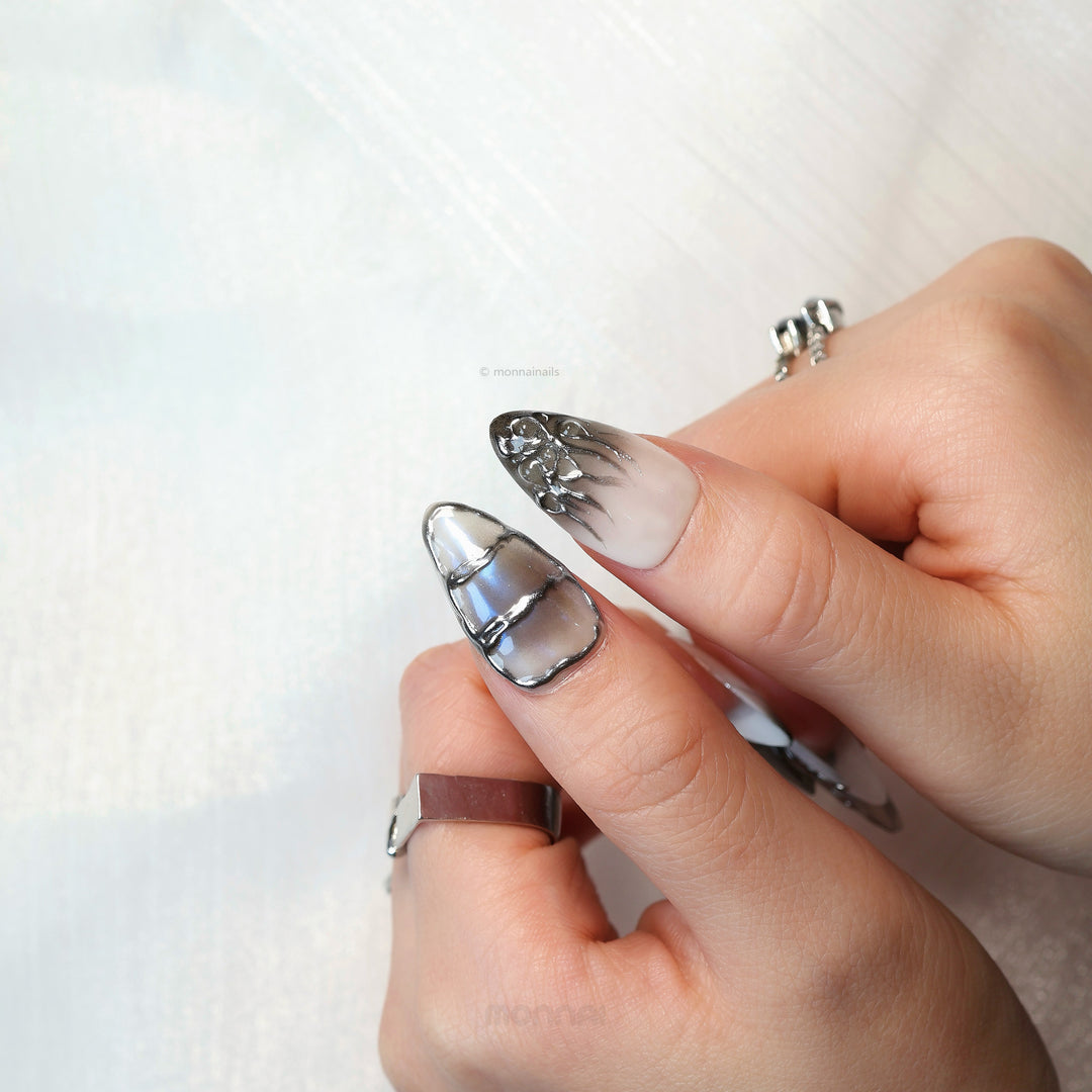 Metal Blaze press-on nails worn on hand, cool grey with chrome edging and flame-like silver detailing