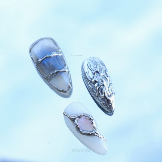 Metal Blaze press-on nails laid out in close-up, with cool grey tones and silver chrome flame detailing