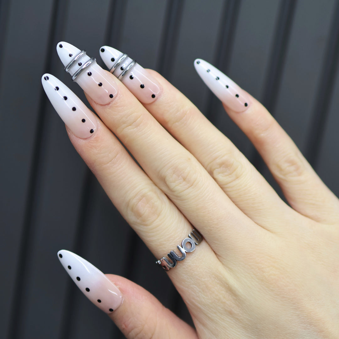 Metal Dot press-on nails on hand with sheer nude base, black polka dots, and silver chrome rings.