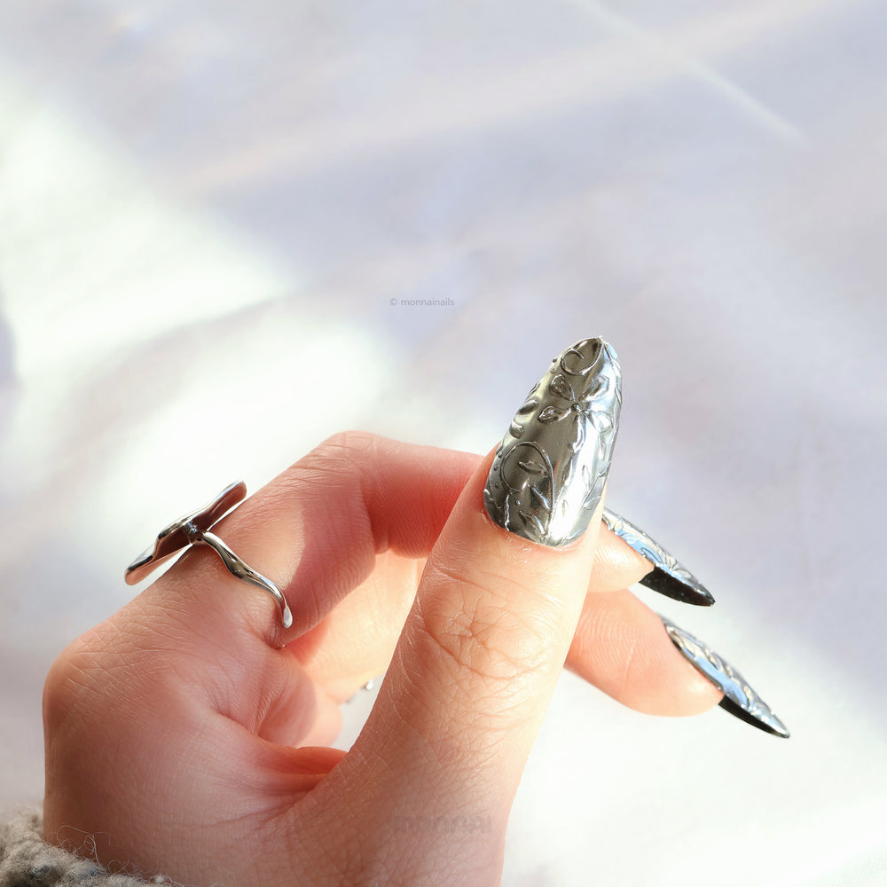 Metallic Bloom press-on nails worn on hand, showing reflective silver chrome floral engraving and sculptural 3D linework