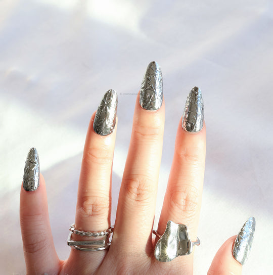 Metallic Bloom press-on nails with reflective silver chrome and raised floral engraving worn on hand