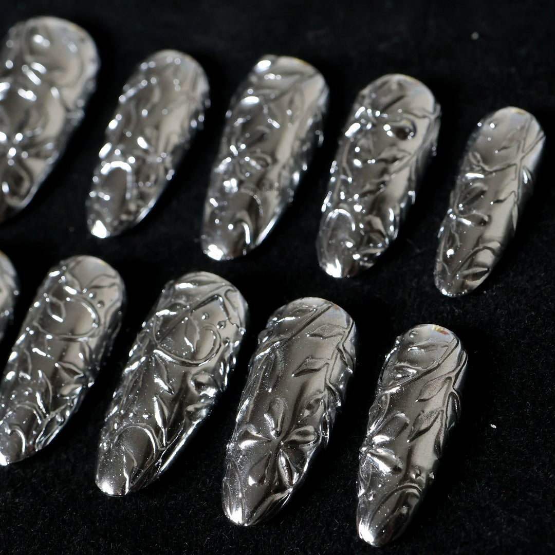 Metallic Bloom press-on nails in close-up, showing reflective silver chrome with sculptural floral engraving.