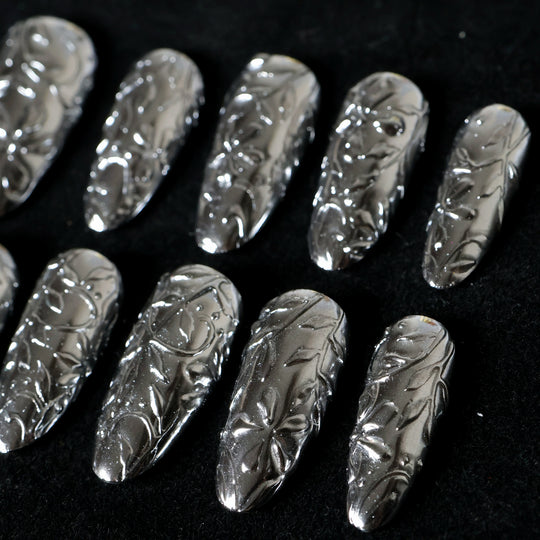 Metallic Bloom press-on nails in close-up, showing reflective silver chrome with sculptural floral engraving.