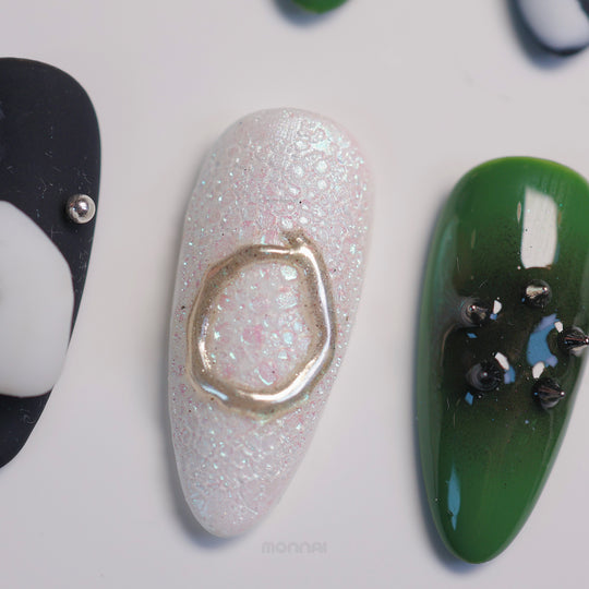 Metallic Mist press-on nails laid out in close-up, showing a sculptural iridescent nail with metallic accents and olive green tones.
