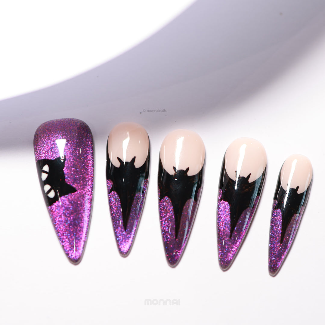 Midnight Bat press-on nails laid out, showing nude bases with black bat silhouettes and shimmering purple cat-eye tips.