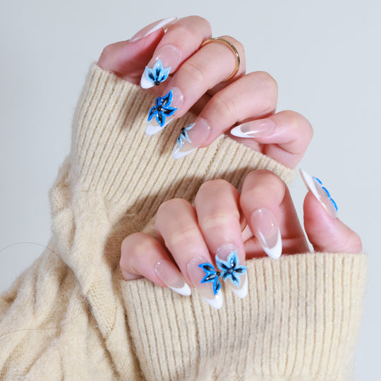 Close-up of hands showcasing Midnight Petals press on nails with electric blue flowers on white French tips.