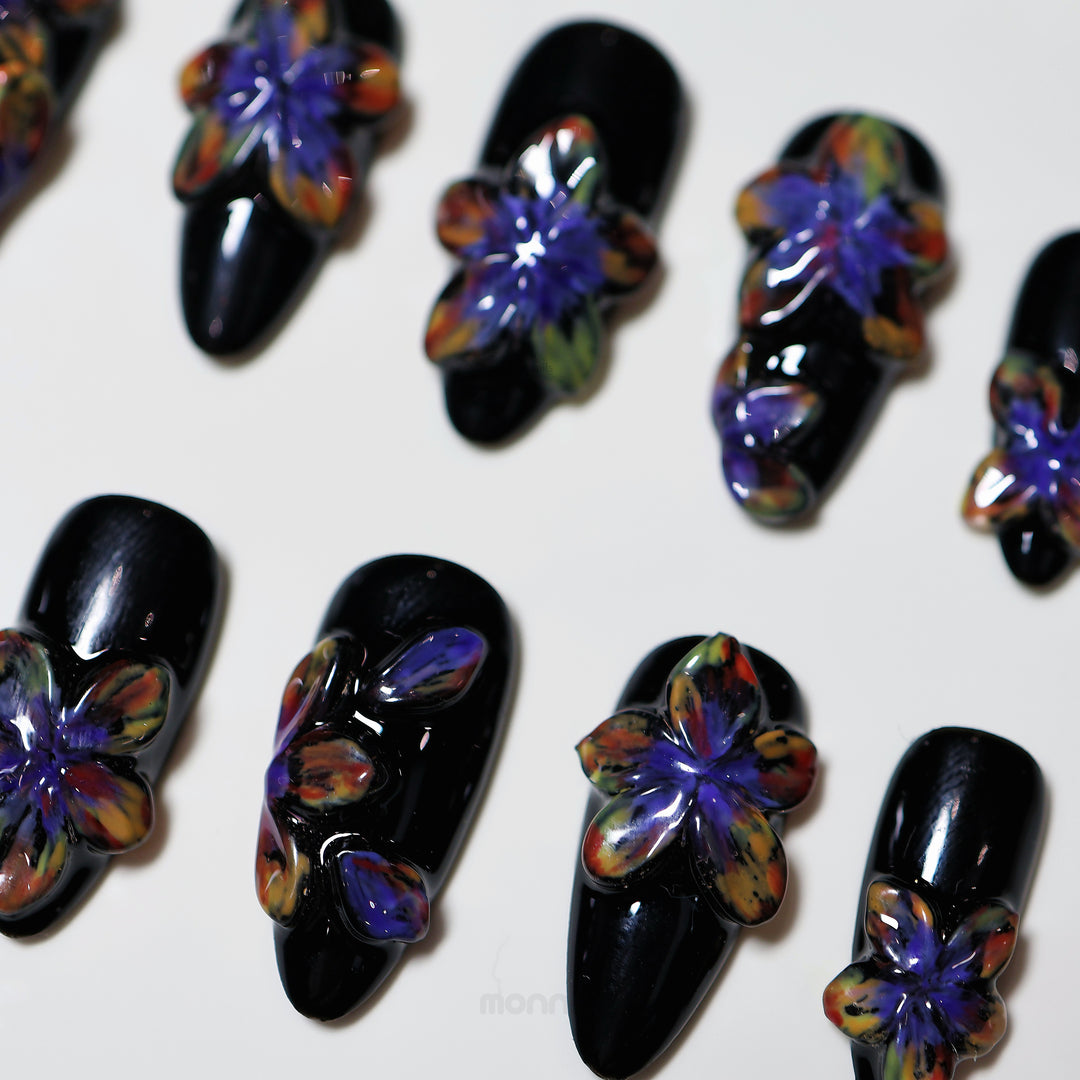 Midnight Violet press-on nails laid out in close-up, with glossy black bases and bold sculpted 3D flowers in shifting tones.