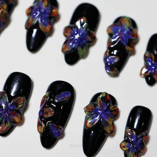 Midnight Violet press-on nails laid out in close-up, with glossy black bases and bold sculpted 3D flowers in shifting tones.