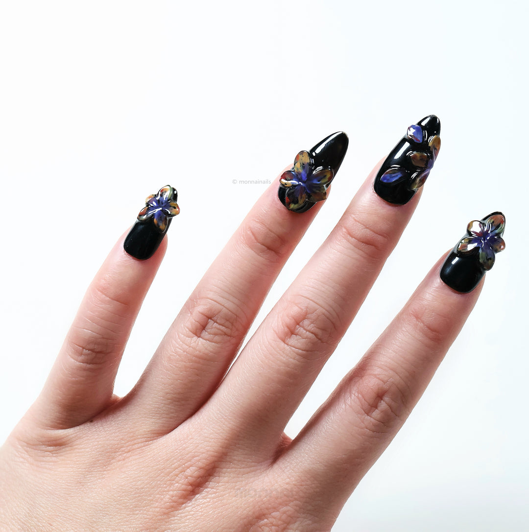 Midnight Violet press-on nails worn on hand, black base with glossy 3D floral accents and shifting violet tones