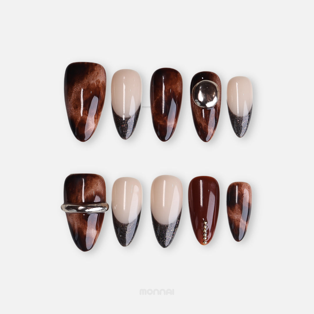 Molten Caramel press-on nails shown laid out with espresso cat-eye shimmer, nude tips, glitter French details, and metallic accents