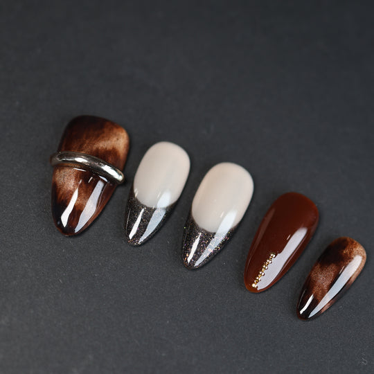 Molten Caramel press-on nails laid out with espresso cat-eye shimmer, glitter French tips, and silver metallic accents.