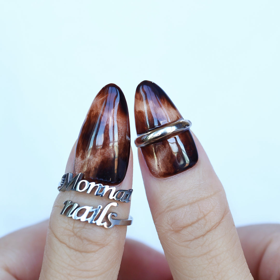 Molten Caramel press-on nails worn on hands, showing espresso cat-eye shimmer and metallic silver band accents.