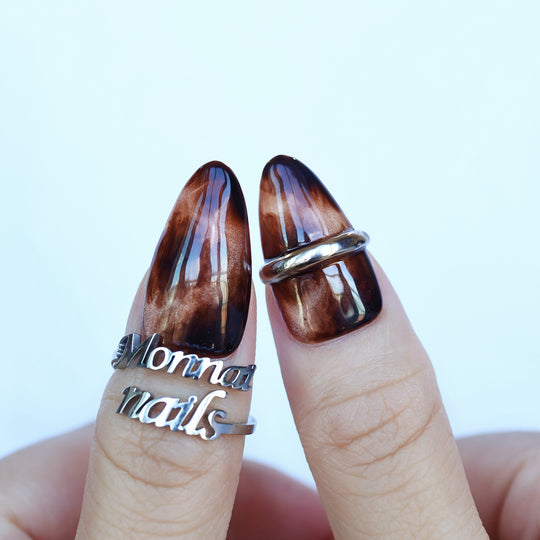 Molten Caramel press-on nails worn on hands, showing espresso cat-eye shimmer and metallic silver band accents.