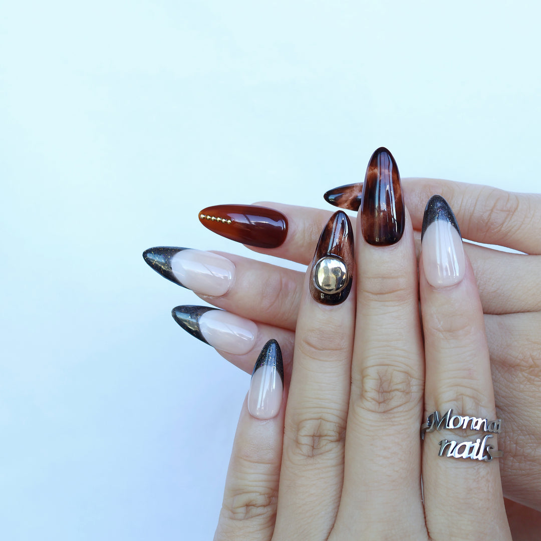 Molten Caramel press-on nails worn on hands, with espresso cat-eye shimmer, nude bases, and dark glitter French tips.