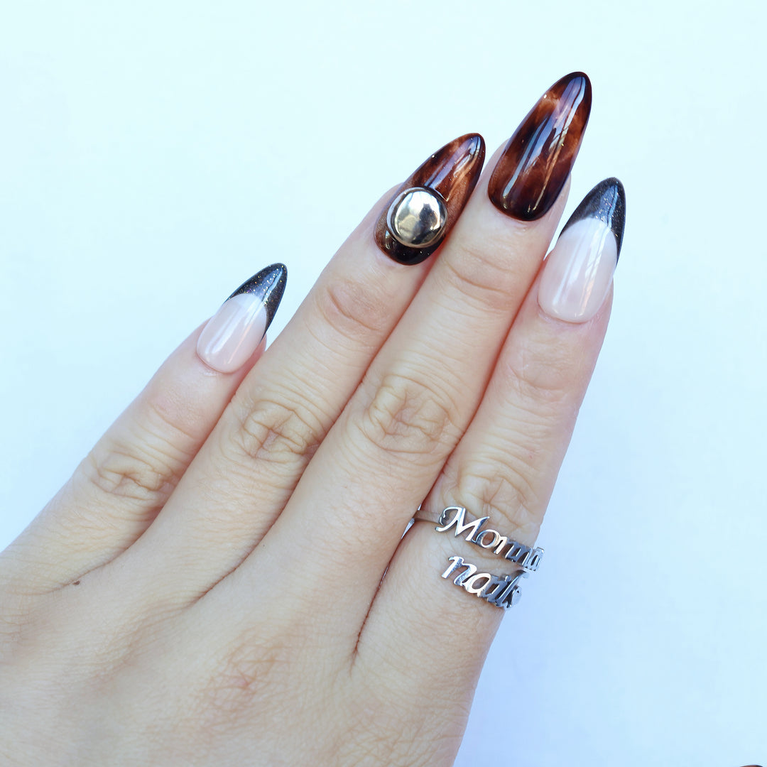 Molten Caramel press-on nails worn on hand, with espresso cat-eye shimmer, nude bases, dark French tips, and a silver dome stud.