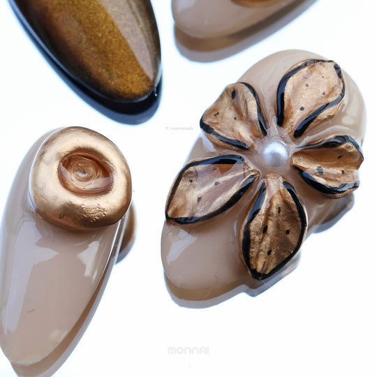 Molten Gold press-on nails shown in close-up, with brown and gold cat-eye shimmer and sculpted floral details.
