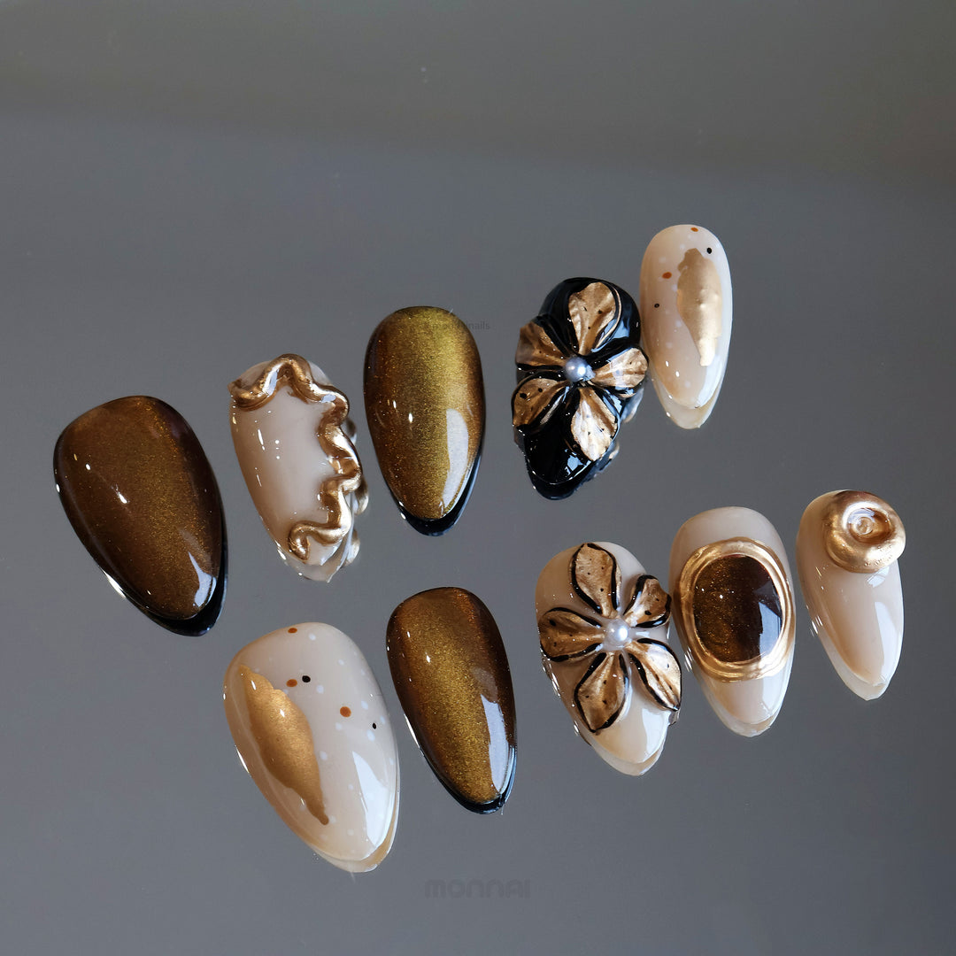Molten Gold press-on nails laid out with brown-gold cat-eye shimmer, floral accents, and glossy metallic details