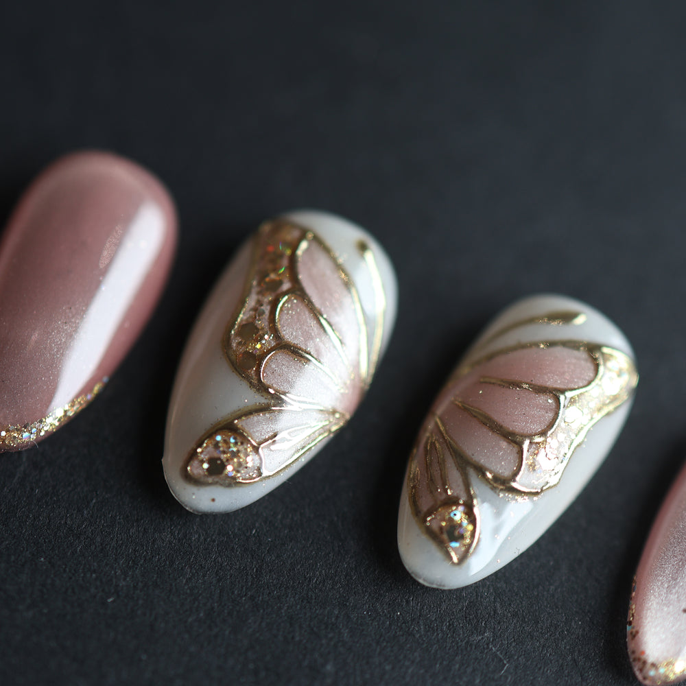 Moonlit Butterfly press-on nails, close-up of soft pink cat-eye and white butterfly wing accents with gold chrome and glitter.