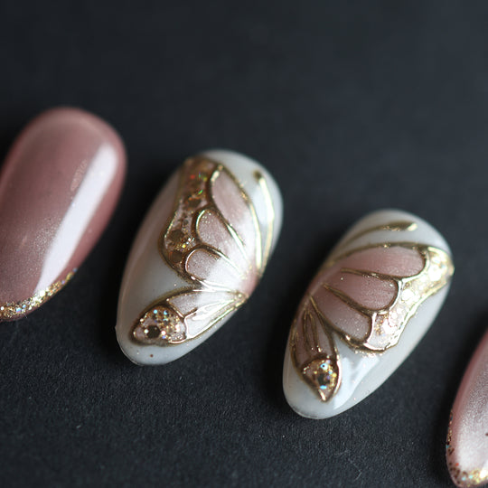 Moonlit Butterfly press-on nails, close-up of soft pink cat-eye and white butterfly wing accents with gold chrome and glitter.