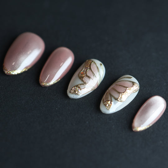 Moonlit Butterfly press-on nails laid out, soft pink cat-eye with gold butterfly wing accents and glitter.