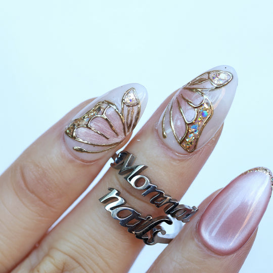 Moonlit Butterfly press-on nails worn on hand, soft pink fairycore butterfly wings with gold chrome outlines and glitter accents.