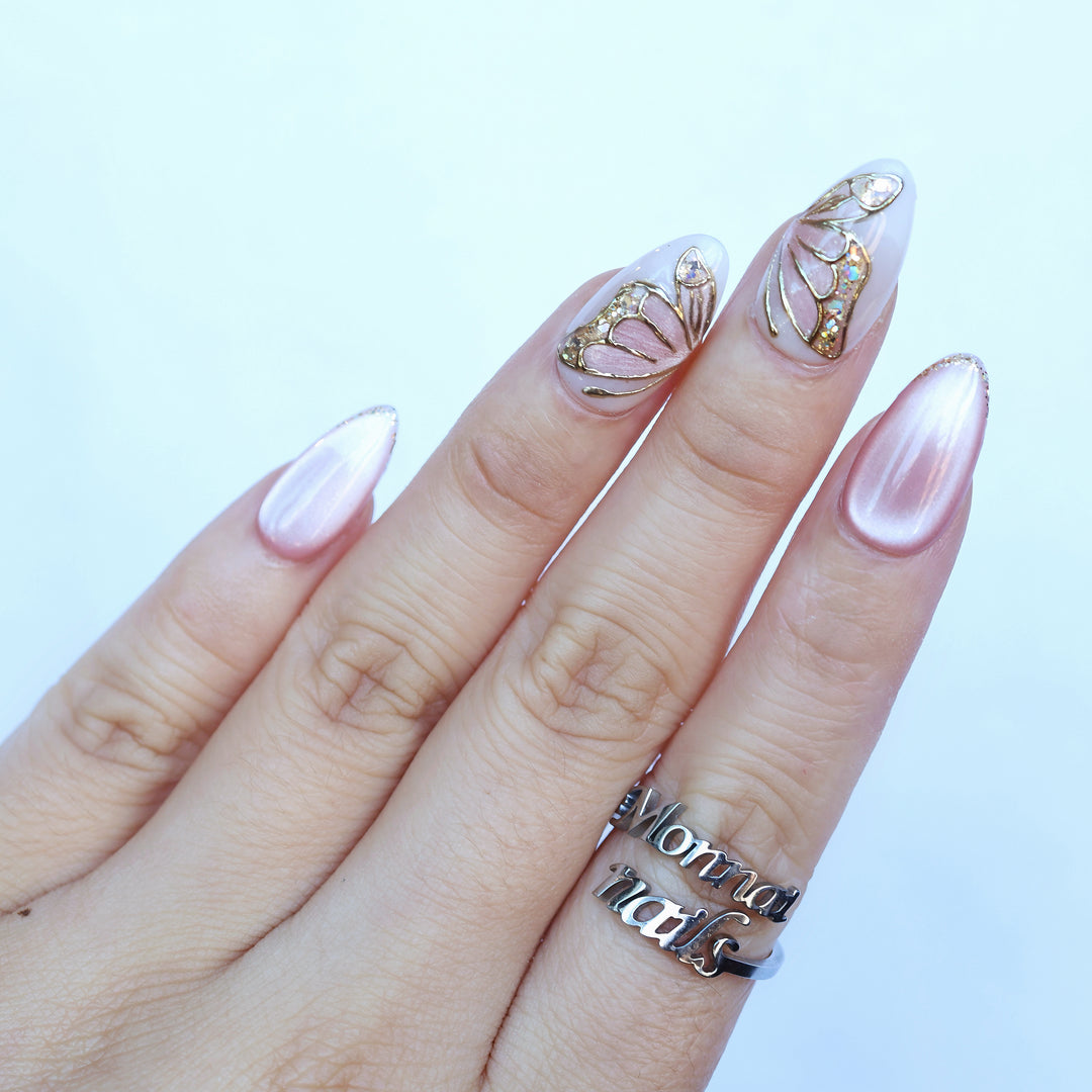 Moonlit Butterfly press-on nails worn on hand, soft pink cat-eye nails with butterfly wing accents and gold chrome outlines.