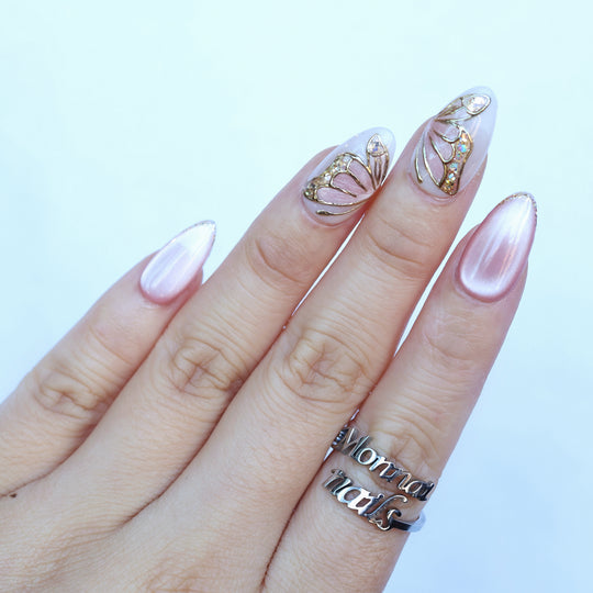 Moonlit Butterfly press-on nails worn on hand, soft pink cat-eye nails with butterfly wing accents and gold chrome outlines.