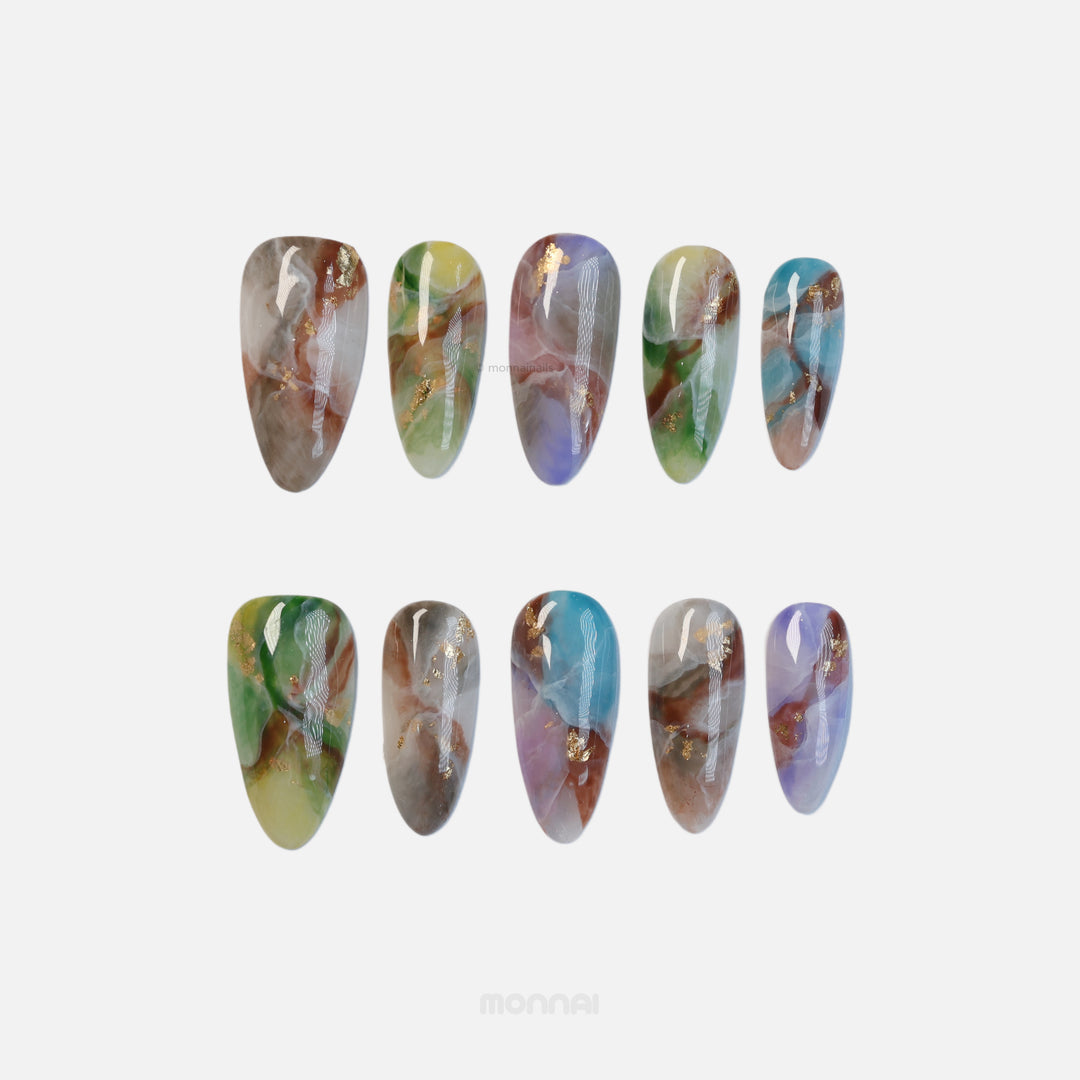 Mystic Marble press-on nails laid out, showing dreamy multicolor watercolor marble swirls with gold foil flakes