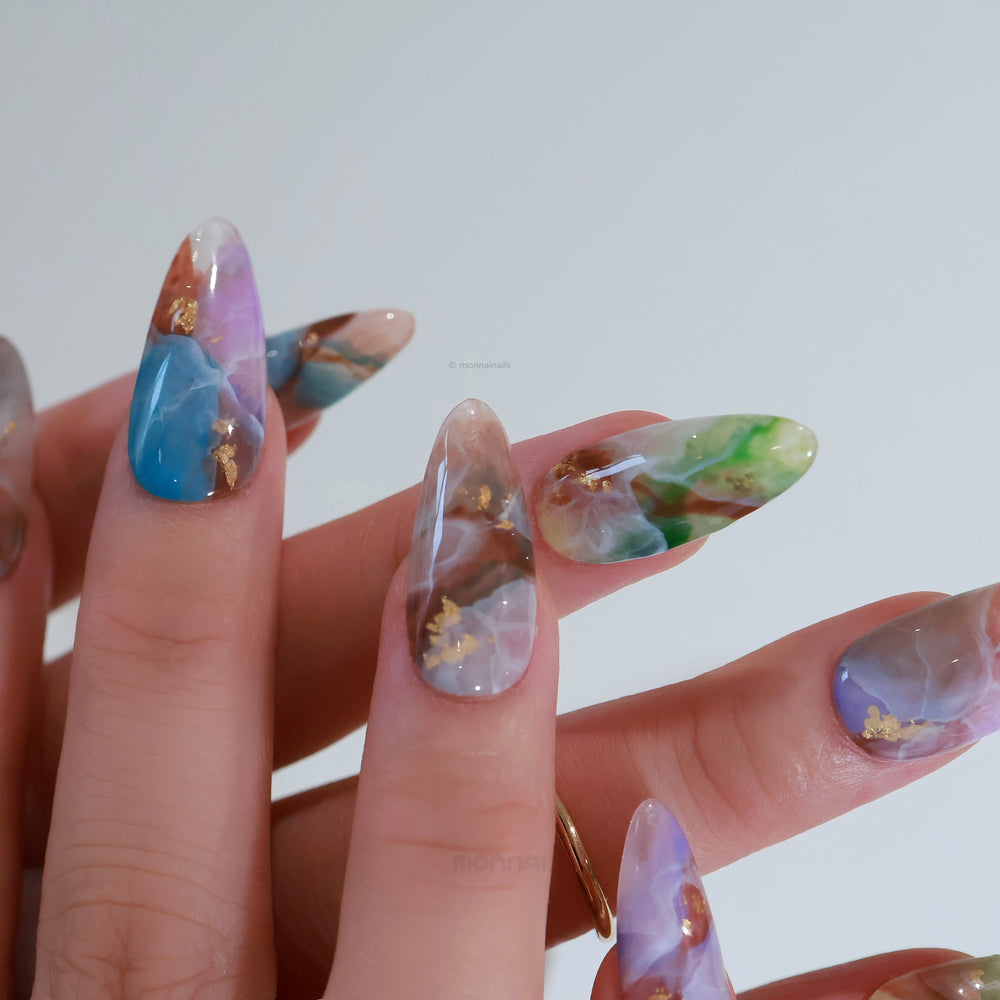 Mystic Marble press-on nails worn on hand, with dreamy watercolor marble swirls and gold foil flakes in a glossy finish.