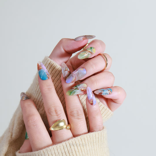 Mystic Marble press-on nails worn on hands, showing dreamy watercolor marble swirls with gold foil flakes.
